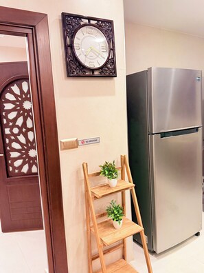 Una cocina con un refrigerador de acero inoxidable, un reloj de pared y un estante de madera con plantas en macetas.