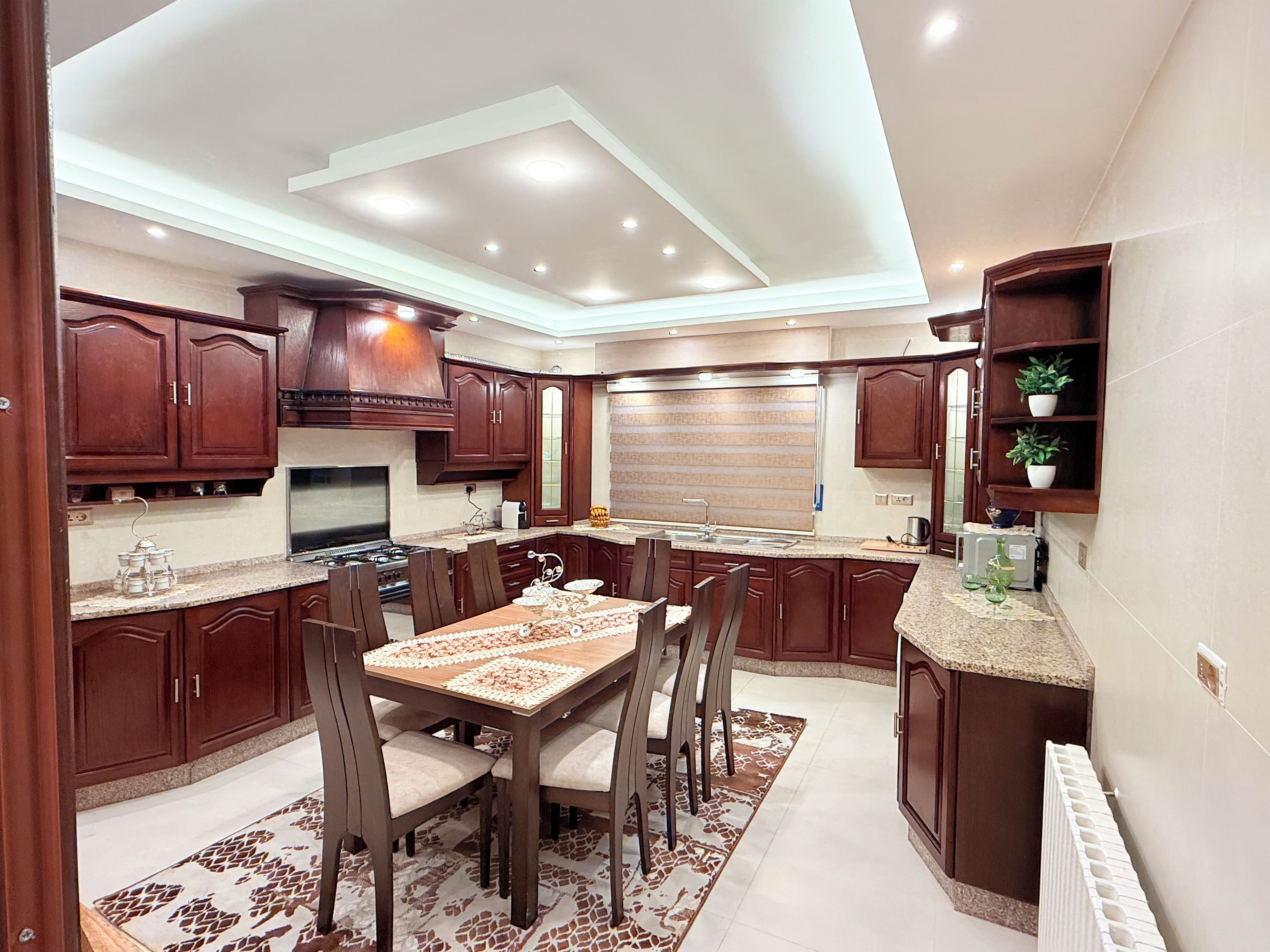 A modern kitchen with dark wood cabinets, a central island, and a dining area with chairs.