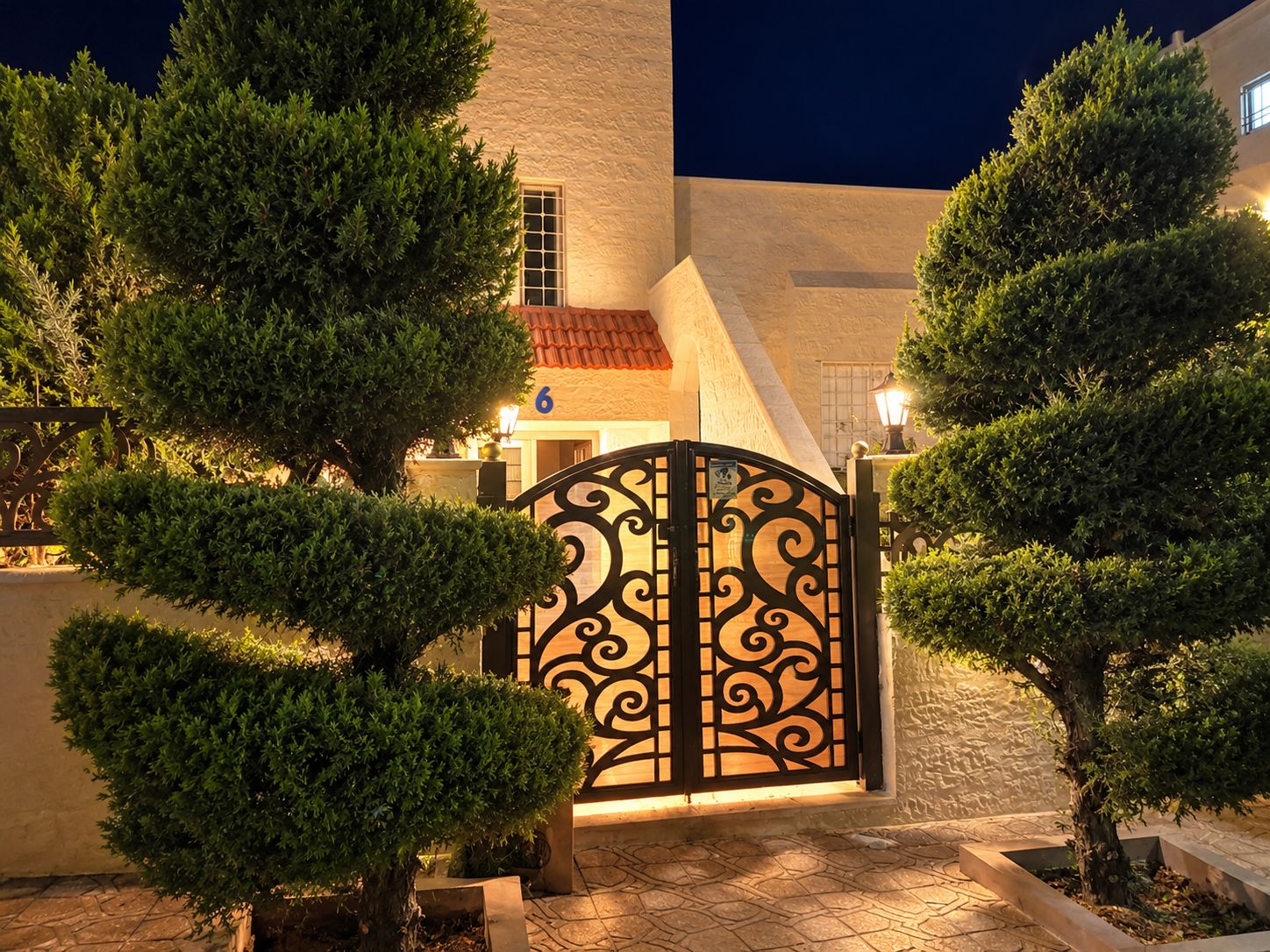 A gated courtyard with trimmed trees and a building with a tiled roof.