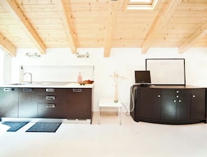A modern kitchen with a white countertop, dark cabinets, and a black island. There is a small white table with a vase of dried plants. - Rialto - Bright Roof Studio (Venezia)