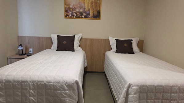 A hotel room with two beds, a nightstand with a lamp, and a painting on the wall.