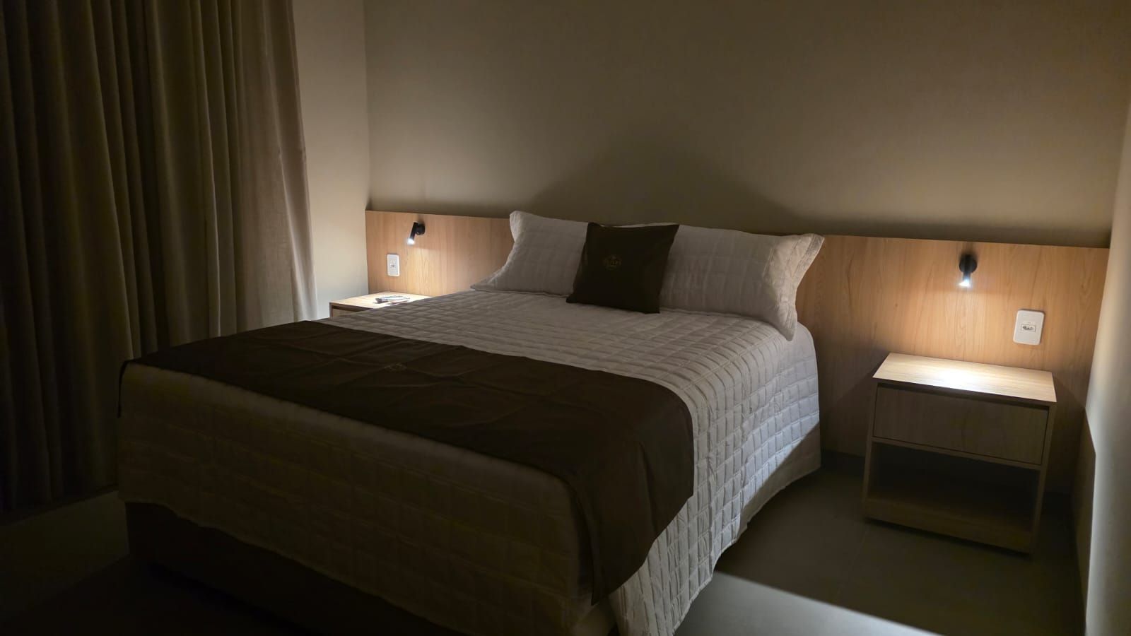 Una habitación de hotel con una cama grande, dos mesitas de noche y una lámpara de noche.