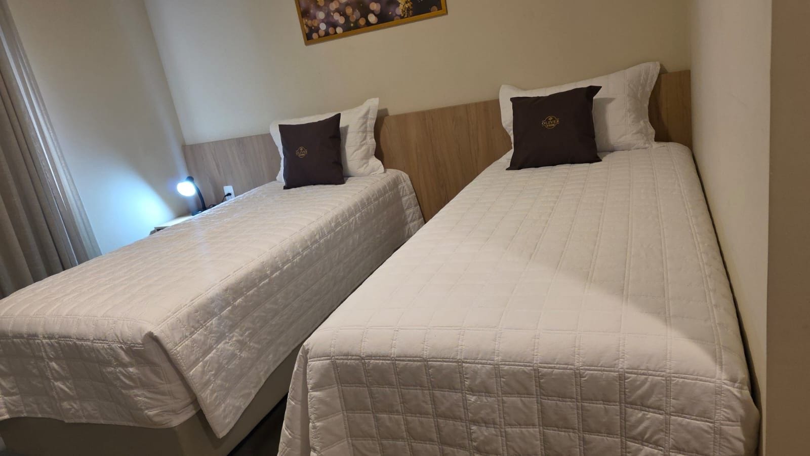 Dos camas individuales con cabeceras, una mesita de noche y una lámpara de pared.