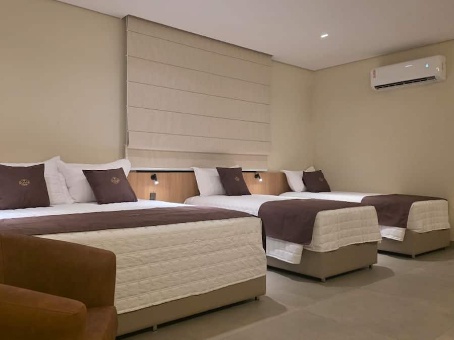 Una habitación de hotel con tres camas, un sofá y un equipo de aire acondicionado.