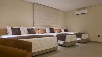 Una habitación de hotel con tres camas, un sofá y un equipo de aire acondicionado.