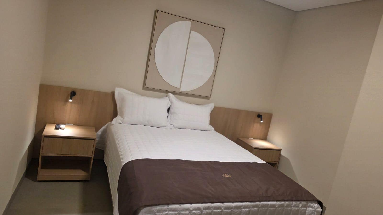 A hotel room with a bed, two bedside tables, and a wall-mounted light fixture.