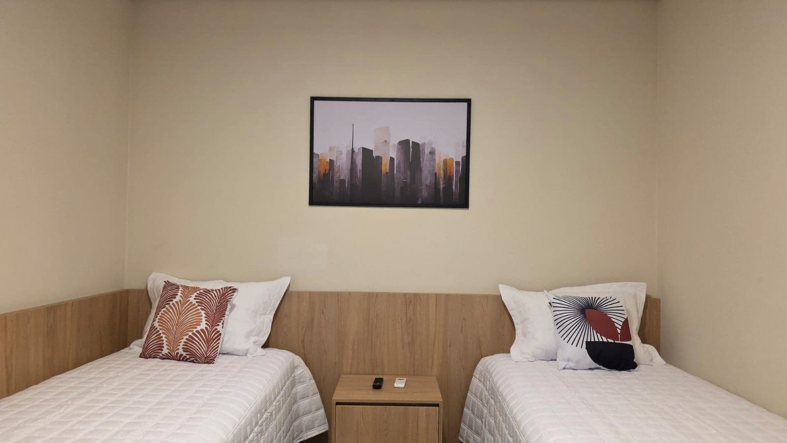 Una habitación de hotel con dos camas, una mesita de noche y un cuadro de un paisaje urbano en la pared.
