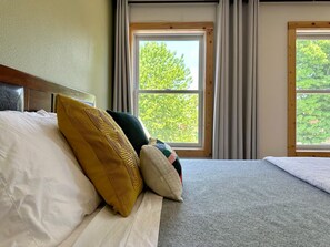Ein Hotelzimmer mit einem Bett, Kissen, einem Kopfteil und zwei mit Vorhängen versehenen Fenstern.