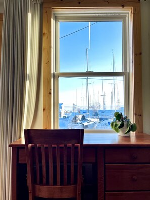 Ein Holztisch mit einem Stuhl, ein Fenster mit Blick auf Boote und ein Blumentopf auf der Fensterbank.