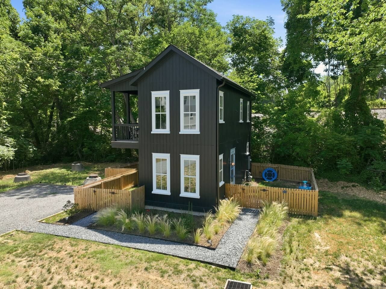 A two-story house with a balcony, surrounded by a wooden fence, and a small garden area with gravel and plants.