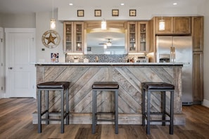 A kitchen with a herringbone wood backsplash, a central island with stools, wooden cabinets, and pendant lighting.