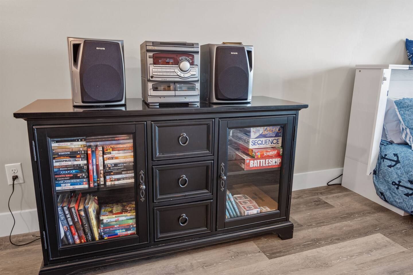 A black entertainment center with two speakers, a glass-fronted cabinet with video games, and a small white appliance in the background.