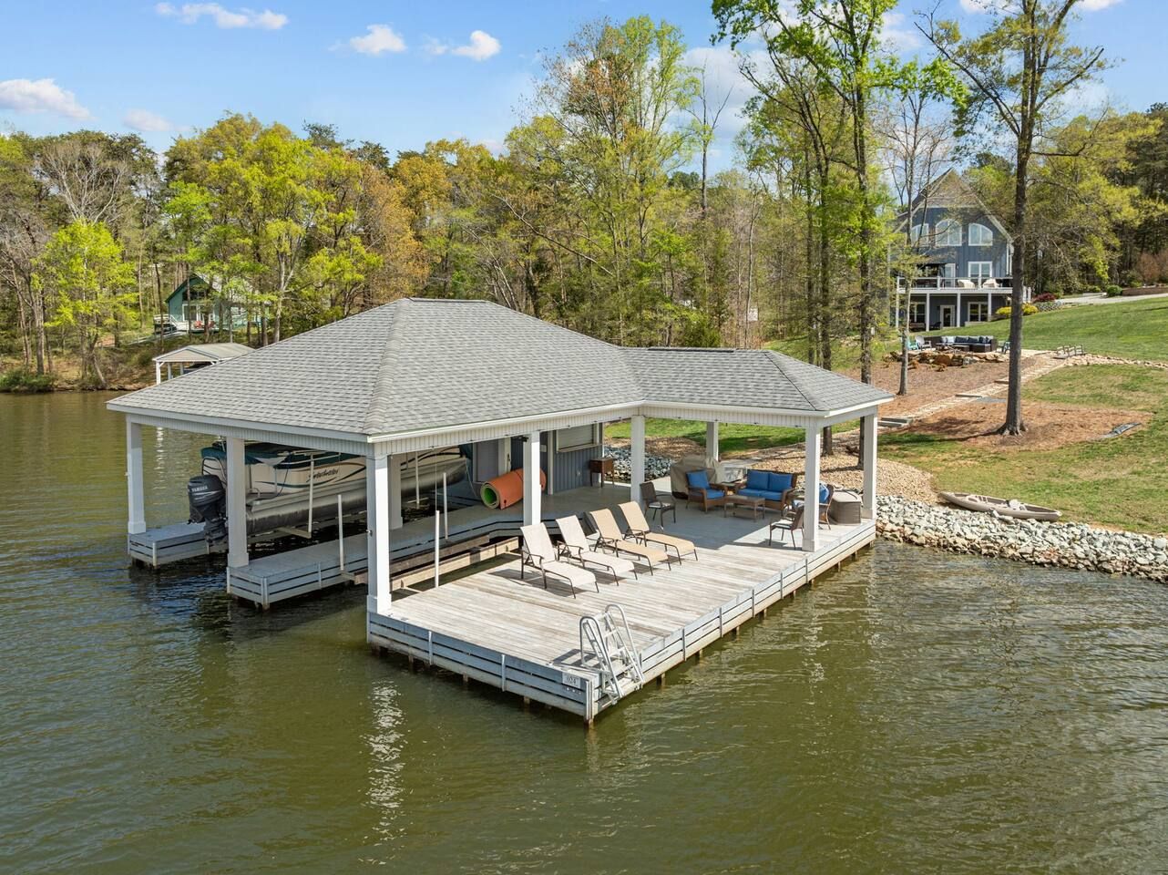 A docked boat house with a covered deck, lounge chairs, and a small boat.