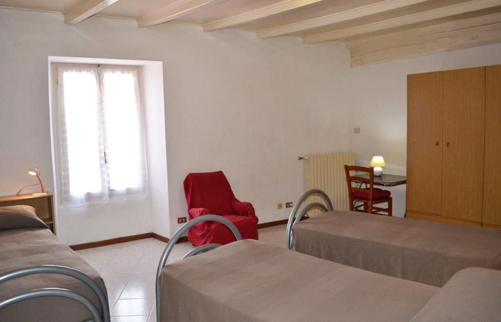 A room with two beds, a red chair, a table with a lamp, and a wardrobe.