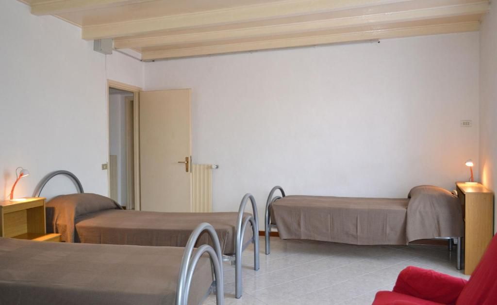 Una habitación con tres camas, una silla roja y una mesita de noche de madera con una lámpara.