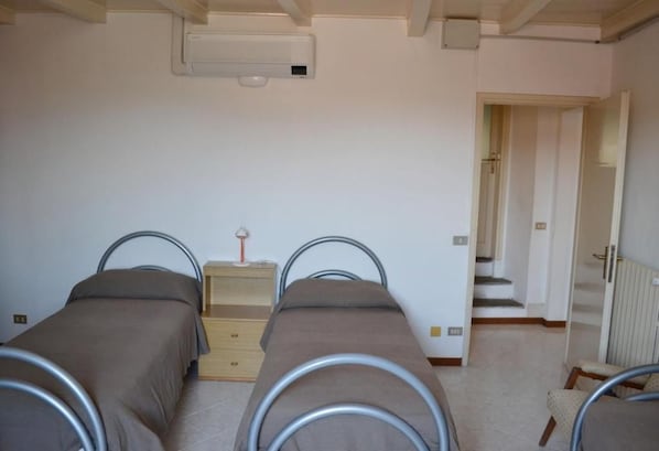 A bedroom with two beds, a dresser, a radiator, and a staircase leading to another room.