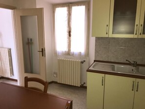 Une cuisine avec un radiateur, une fenêtre avec des rideaux et un évier.