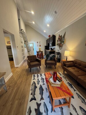 A spacious living room with a wooden floor, a staircase, and a kitchen area with dark cabinets. - 9139 Orange -2-bedroom w/ Loft - Melton Hill Lake & Marina -Close to downtown UT (Oak Ridge)
