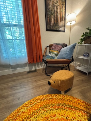 A room with a wooden floor, a chair with a patterned cushion, a small bear-shaped ottoman, and a wall-mounted lamp. - 9139 Orange -2-bedroom w/ Loft - Melton Hill Lake & Marina -Close to downtown UT (Oak Ridge)