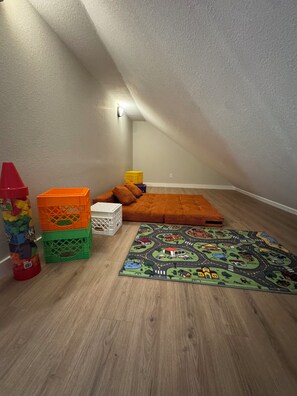A cozy attic room with a sloped ceiling, a colorful play mat, and storage bins. - 9139 Orange -2-bedroom w/ Loft - Melton Hill Lake & Marina -Close to downtown UT (Oak Ridge)