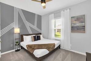 Ein Schlafzimmer mit Bett, Deckenventilator, Fenster mit Jalousien und einem Bild an der Wand.