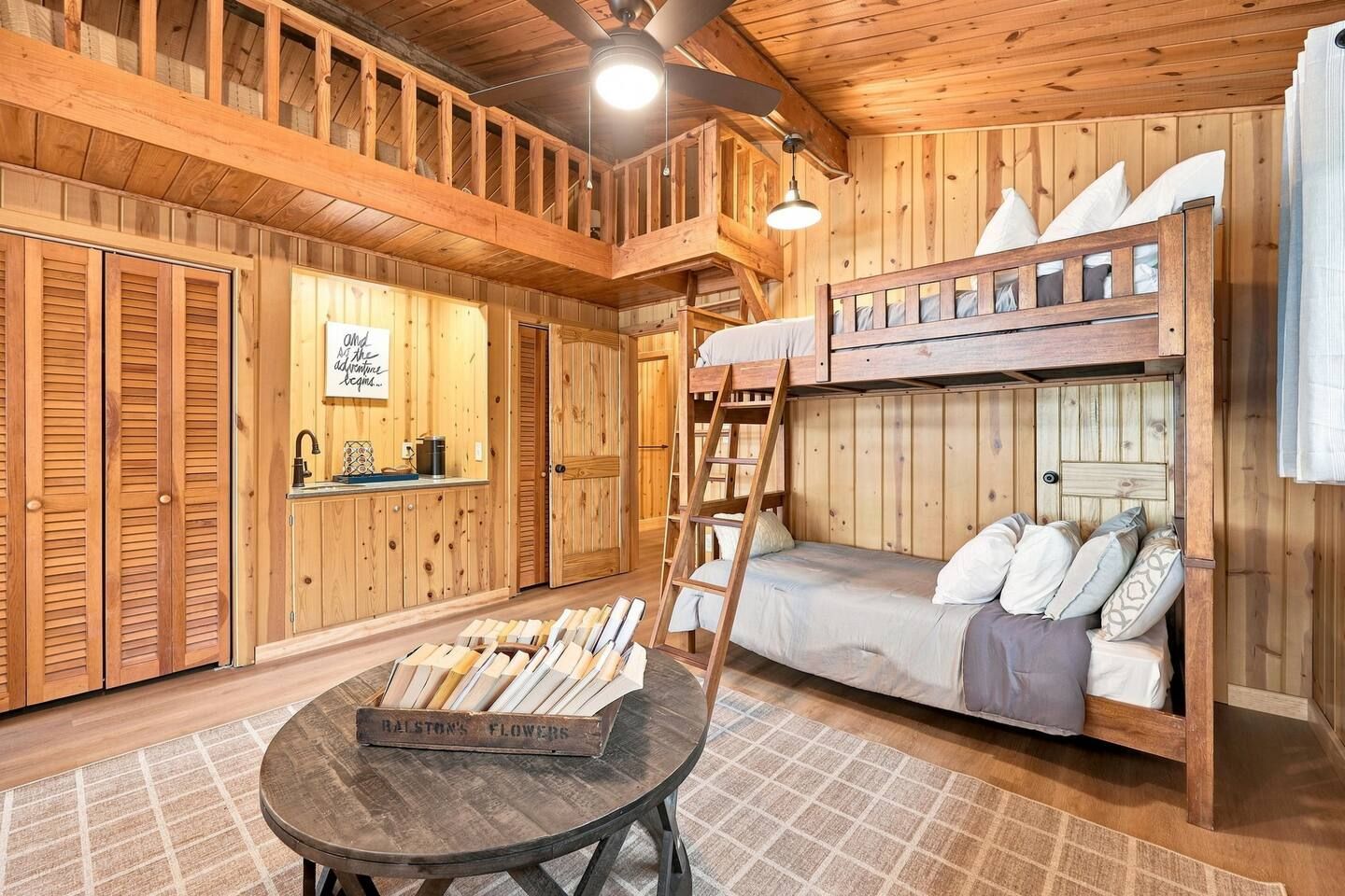 L’intérieur d’un chalet en bois, avec des lits superposés, une table agrémentée d’un arrangement floral et un panneau accroché au mur.