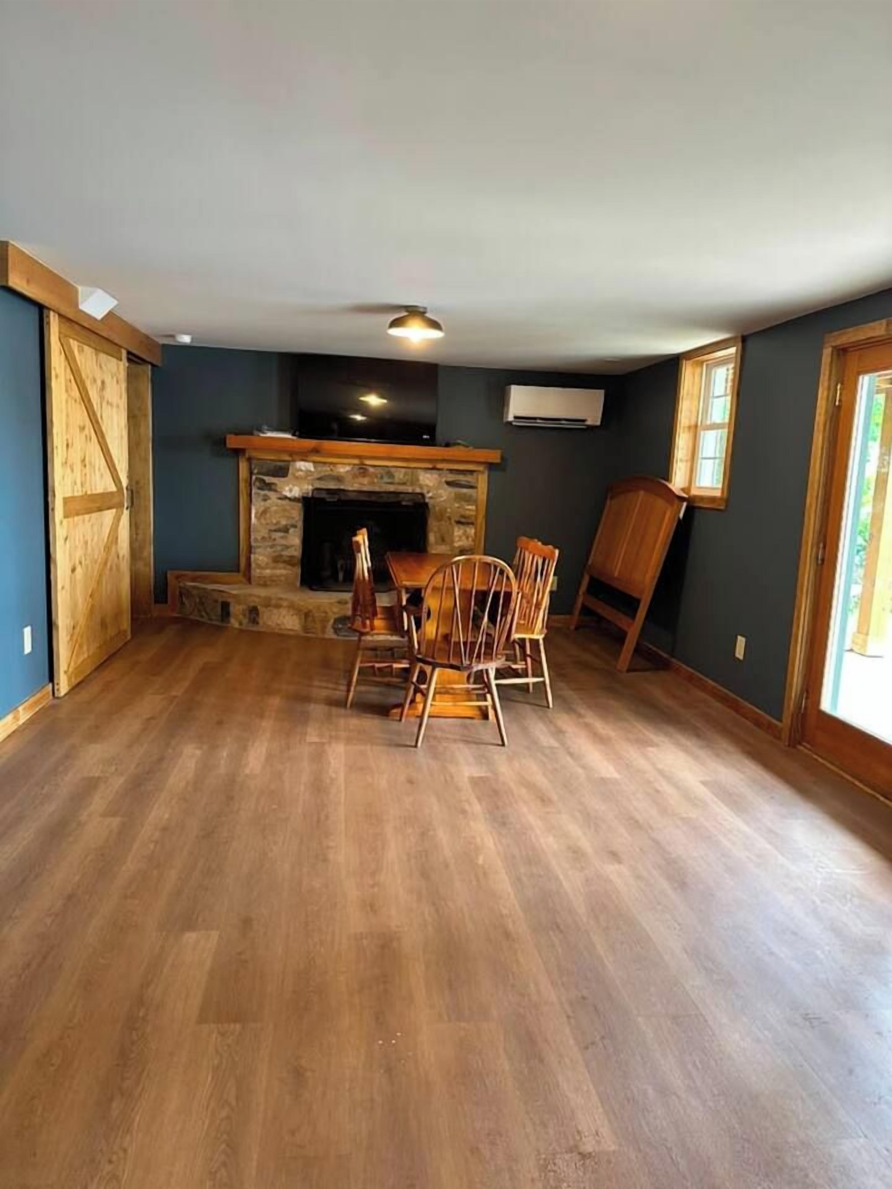 Ein Zimmer mit Kamin aus Stein, Holzboden und einer Essecke mit Stühlen.