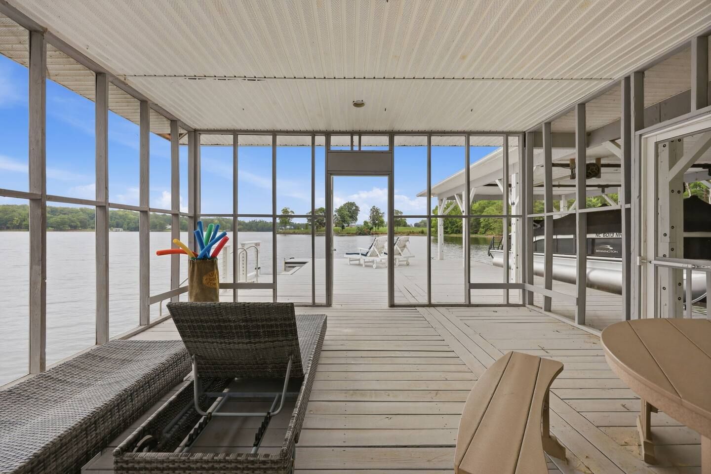 A covered outdoor deck with a view of a body of water, wicker furniture, and a table.