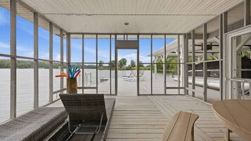 A covered outdoor deck with a view of a body of water, wicker furniture, and a table.