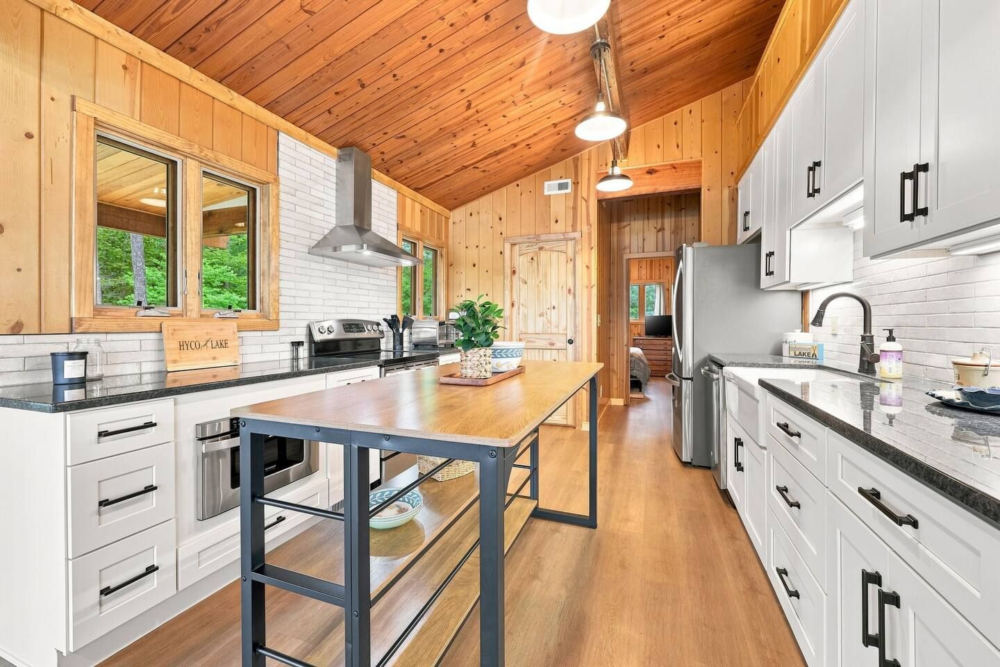 A modern kitchen with wooden cabinets, a central island, and a view of a forested area.