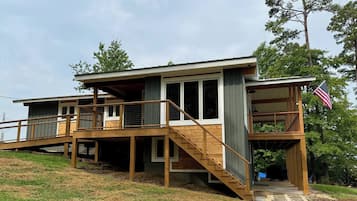 A two-story house with a wooden deck, a staircase, and an American flag.
