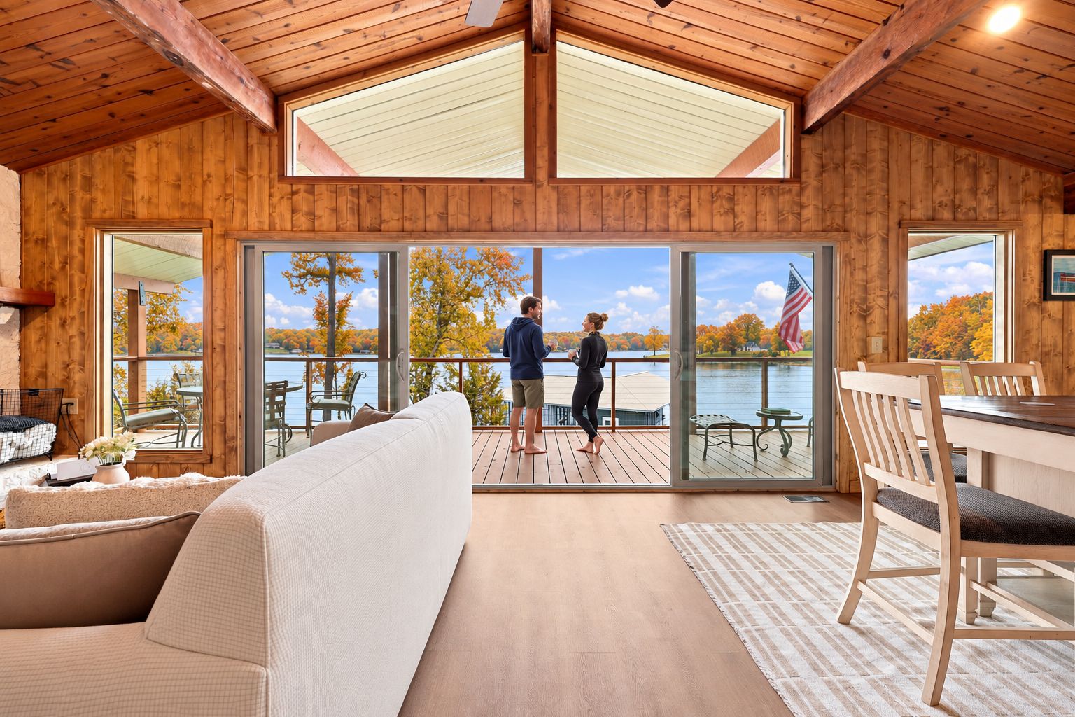 Guests can sink into the cozy sofa and dining table in this sunroom, taking in wide-open lake views through the wall of windows and doors to the deck.