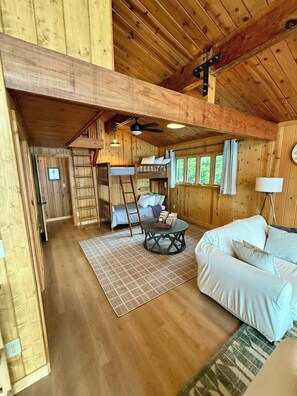 Un interior de madera con una cama litera, un sofá, una mesita de centro y una lámpara.