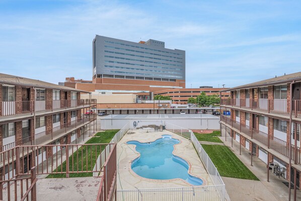A hotel with a central swimming pool, multiple balconies, and a large building in the background.