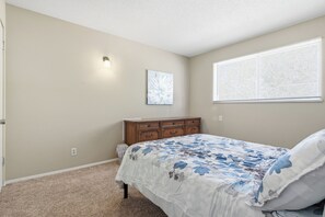 A bedroom with a bed, a dresser, a wall-mounted light, and a window with blinds.