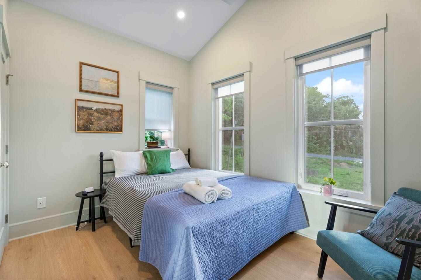 Een slaapkamer met een bed, een stoel, een raam en een schilderij aan de muur.