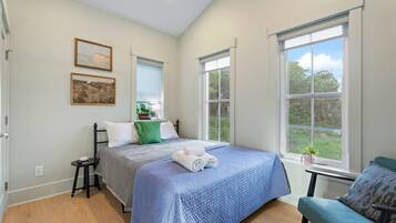 Een slaapkamer met een bed, een stoel, een raam en een schilderij aan de muur.