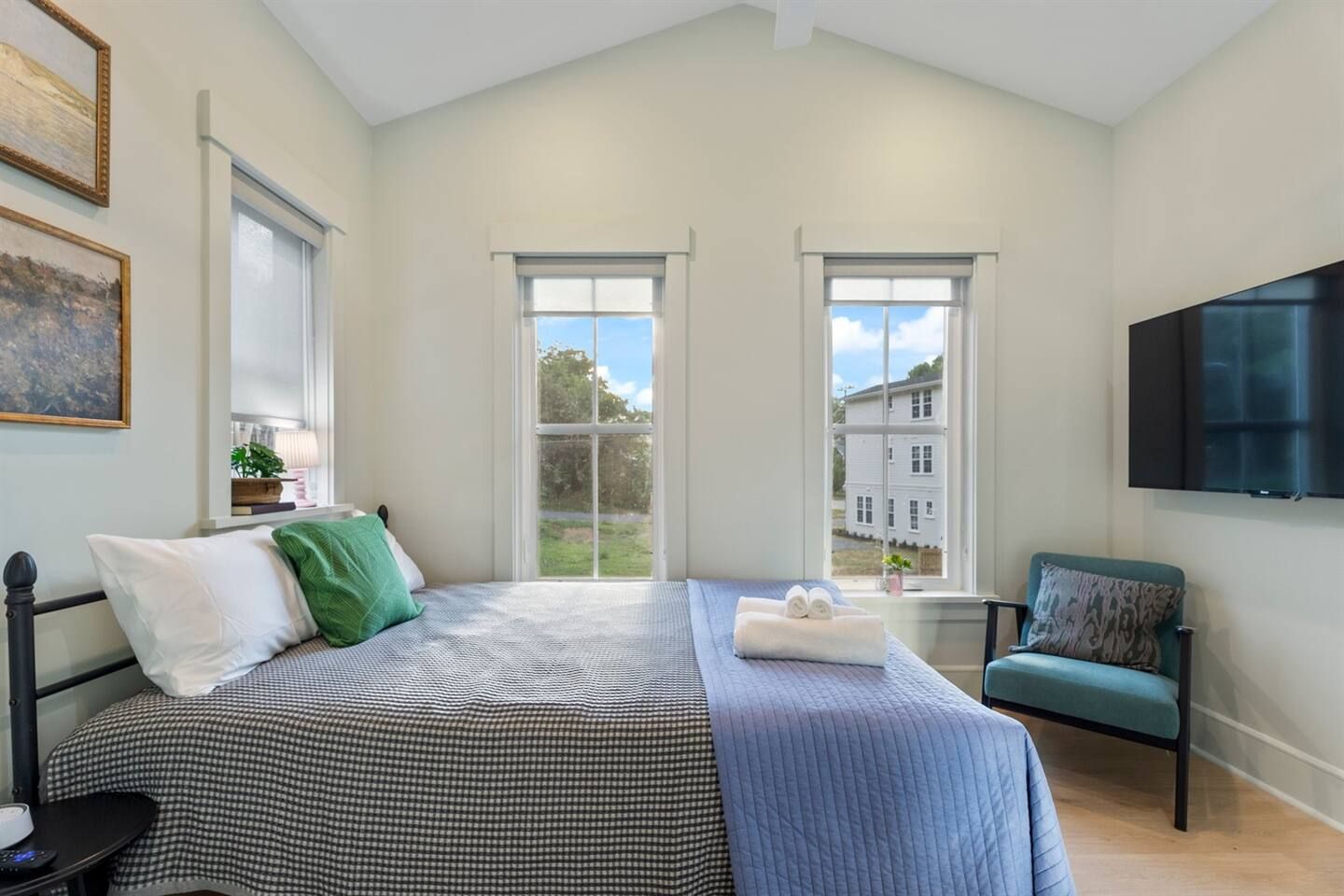 Un dormitorio con cama, una silla, un televisor y ventanas.