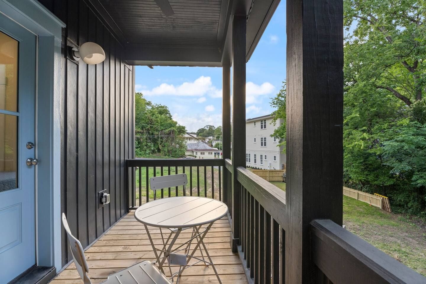 Una terraza de madera con una mesa, sillas, una puerta y vista a una zona residencial.