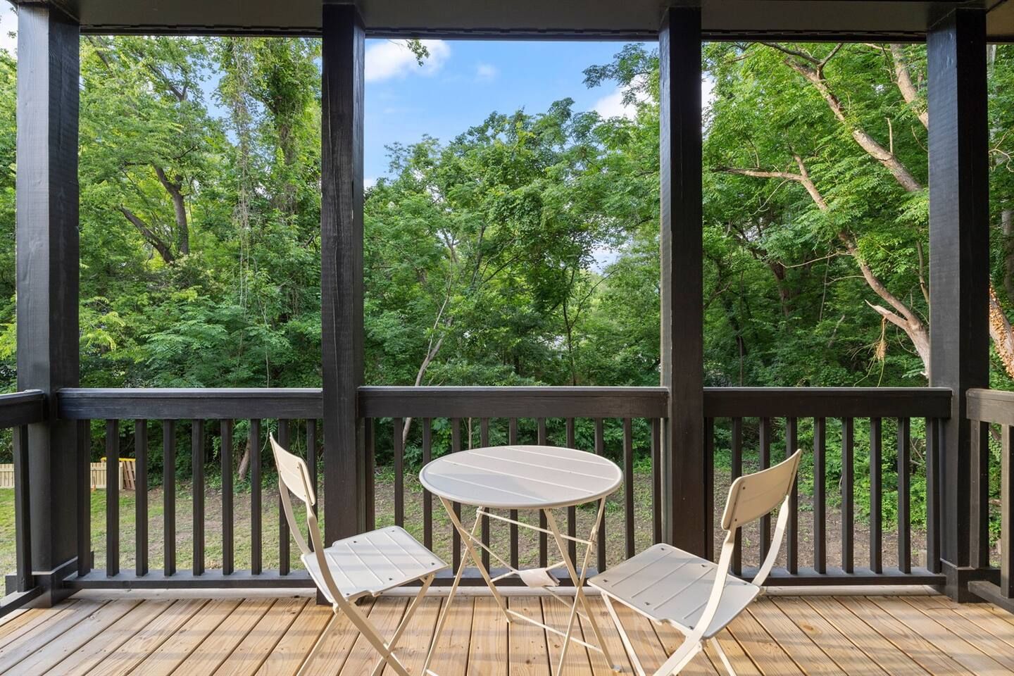 Un espace extérieur abrité, doté d’une table et de chaises, entouré d’une terrasse en bois et offrant une vue sur une végétation luxuriante.