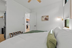 Une chambre à coucher avec un lit, un plaid vert, un tableau et une fenêtre avec des stores.