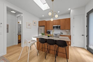 Une cuisine moderne dotée d’un îlot central, de meubles en bois, d’appareils électroménagers en acier inoxydable et d’une verrière.