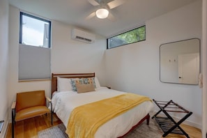 Una camera da letto con un letto, una sedia, una finestra, un condizionatore d'aria, uno specchio e una ventola a soffitto.