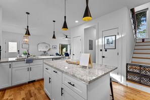 A modern kitchen with white cabinetry, granite countertops, pendant lighting, and a view of the outdoors. - Sky Deck - New Build - Downtown - Fenced - FirePit (Raleigh)