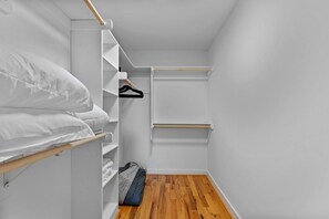 A walk-in closet with wooden flooring, white walls, and a bed with white bedding. - Sky Deck - New Build - Downtown - Fenced - FirePit (Raleigh)