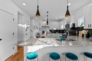 A modern kitchen with white cabinets, a marble island, and bar stools. - Sky Deck - New Build - Downtown - Fenced - FirePit (Raleigh)