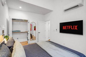 A bedroom with a bed, a wardrobe, a mirror, and a wall-mounted TV displaying the Netflix logo. - 4 Ensuite Flats, Downtown, Architecture, Skyline (Raleigh)
