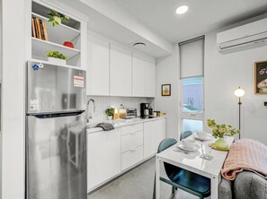 A compact kitchen with white cabinetry, a stainless steel refrigerator, a coffee maker, and a dining area with a table and chairs. - 4 Ensuite Flats, Downtown, Architecture, Skyline (Raleigh)