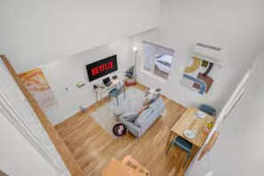 Ein modernes Wohnzimmer mit einem grauen Sofa, einem Couchtisch und einem Fernseher, der 'NETFLIX' anzeigt.