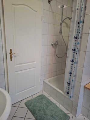 Un baño con ducha, inodoro y una puerta con pomo de latón.